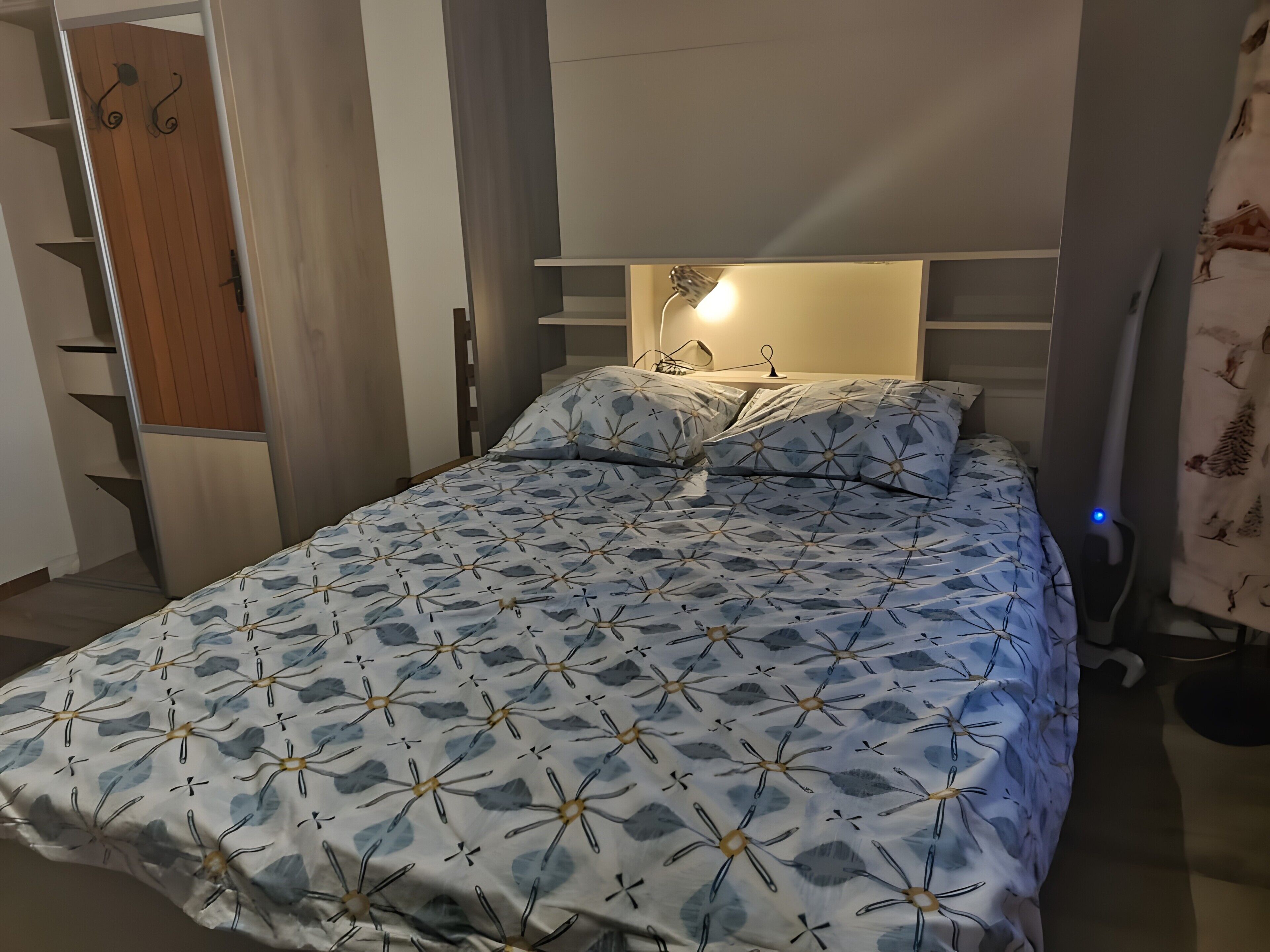 Un dormitori amb un llit, una taula de nit, una làmpada i un armari.
