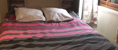 A bed with a patterned bedspread, a bedside lamp, and a framed picture on the wall.