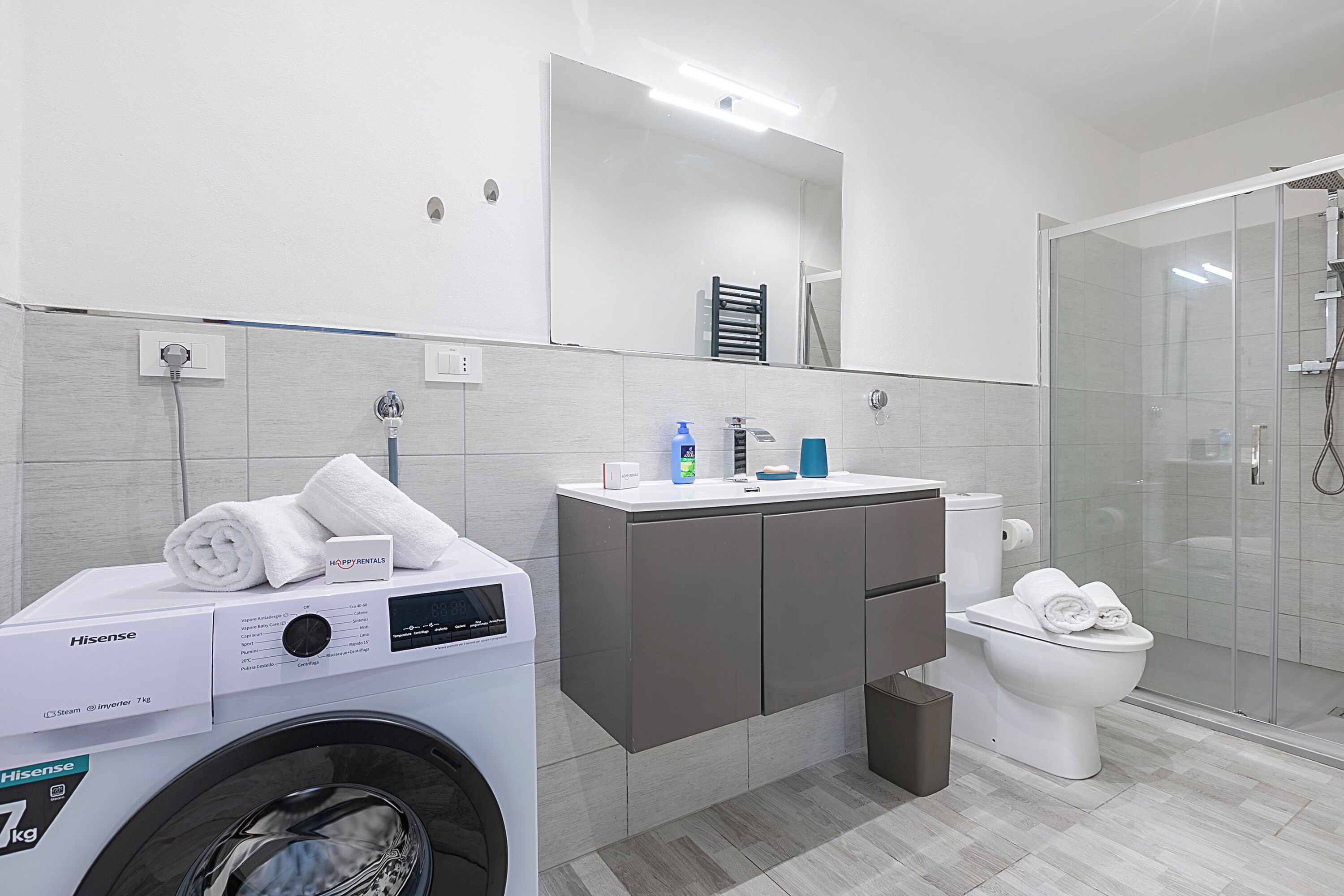 Un baño moderno con lavadora, inodoro, lavamanos y cabina de ducha de vidrio.