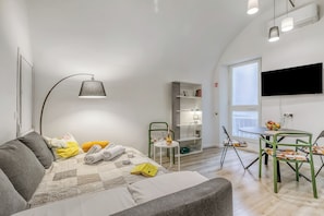 A modern living room with a sofa, a dining table, and a TV mounted on the wall. - Casa di Lilo (Sanremo)