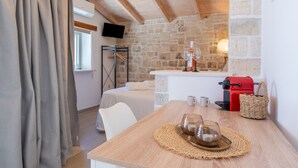 Ein gemütliches Zimmer mit Steinwand, Holzboden, einem Bett, einem Tisch mit Kaffeemaschine und einem an der Wand montierten Fernseher.
