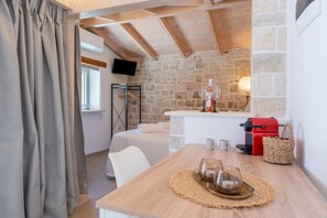 A cozy room with a stone wall, a wooden ceiling, a bed, a table with a coffee maker, and a TV mounted on the wall. - Studio Apartment 'Maestro' with Mountain View, Wi-Fi and Air Conditioning (Gaios)