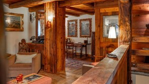 Een rustiek interieur met houten balken, een bank, een eettafel en ingelijste kunstwerken.