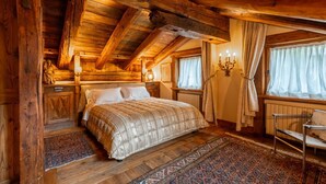 Een slaapkamer in een houten chalet met een bed, nachtkastje, een kroonluchter en een raam met gordijnen.