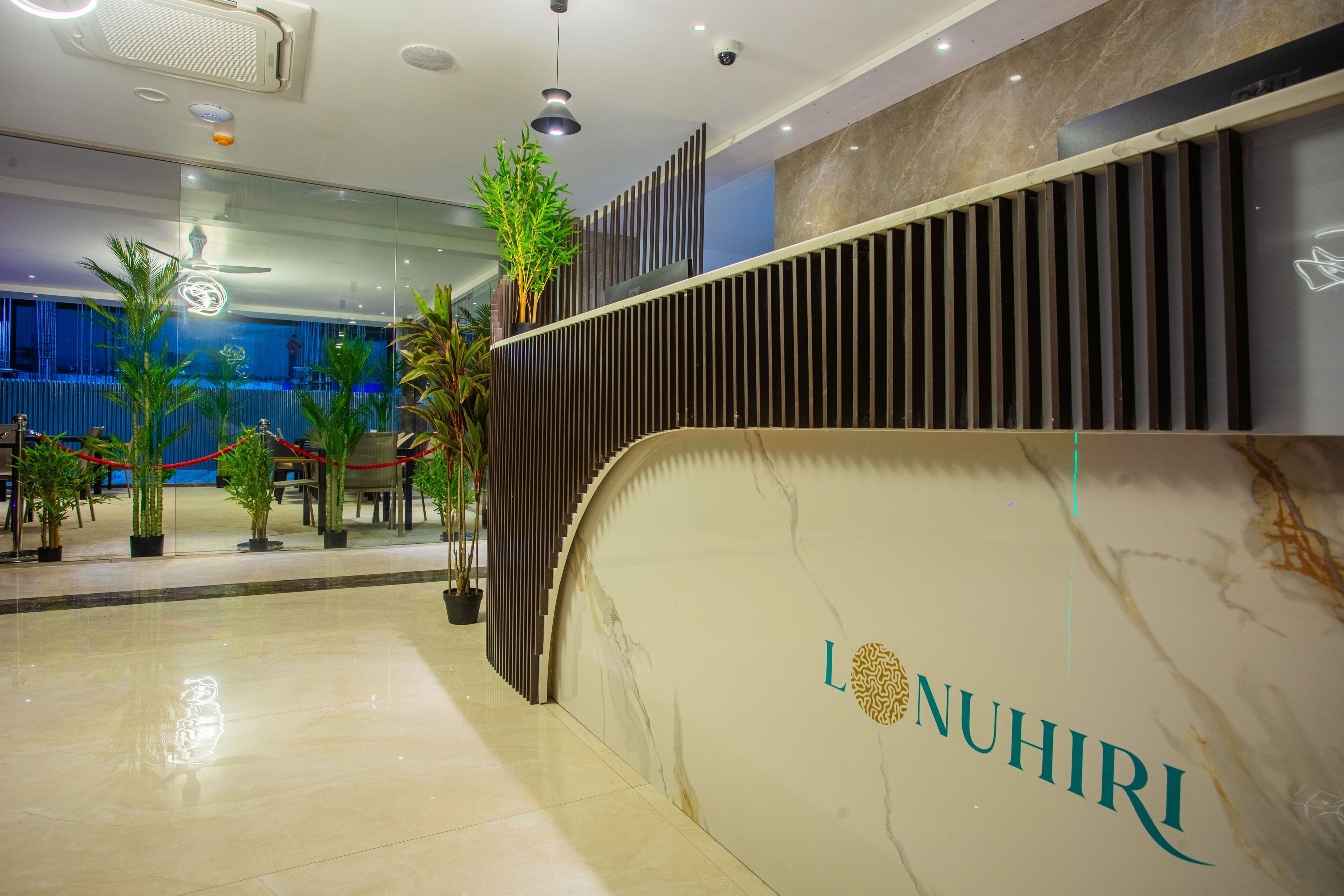 Una moderna zona de recepción con un mostrador de mármol, plantas en macetas y un gran espejo que refleja el interior.