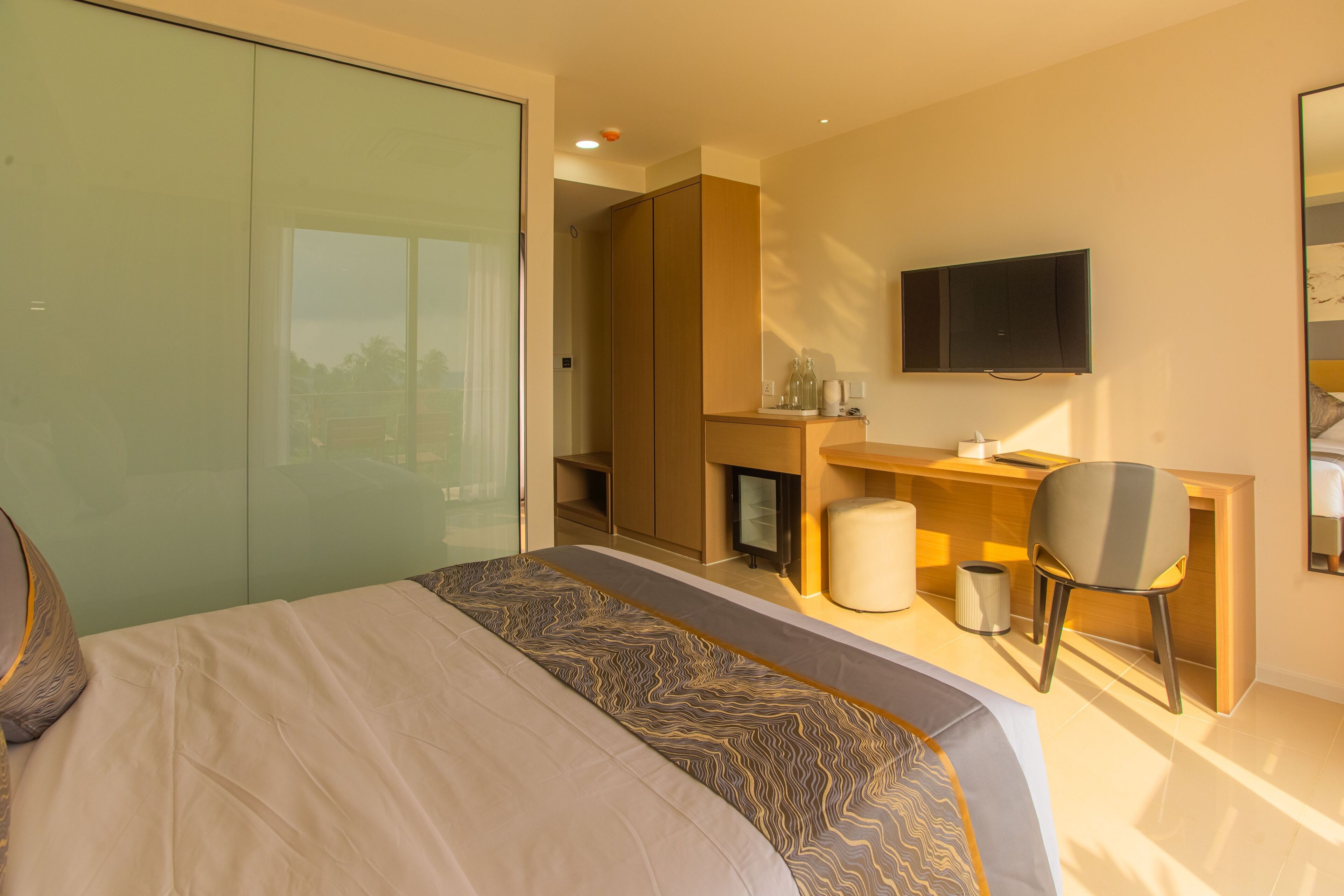 A modern hotel room with a large bed, a desk, a chair, a television, and a wardrobe.