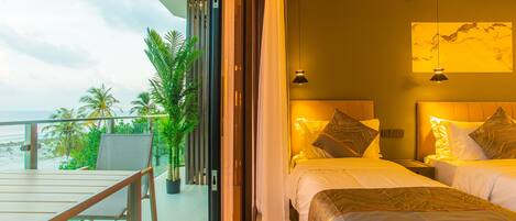 A hotel room with two beds, a balcony with a view of the ocean, and a dining area with a table and chairs.