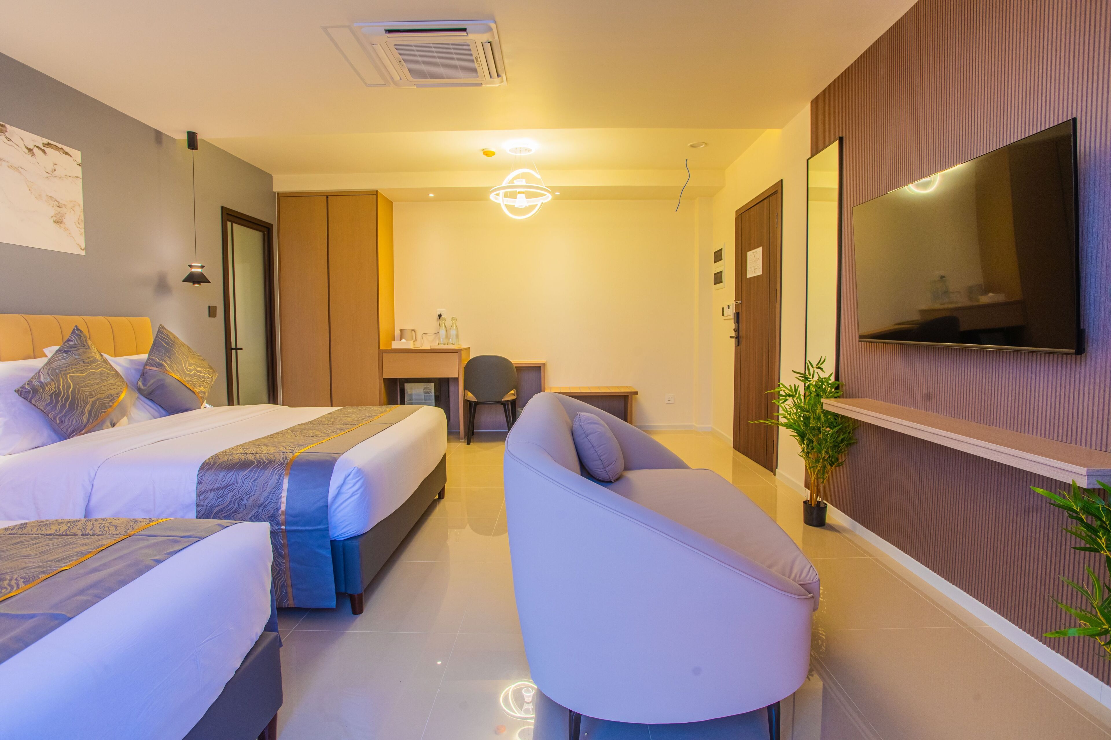 Habitación de hotel con dos camas, un sofá, un escritorio, un televisor y una planta en maceta.