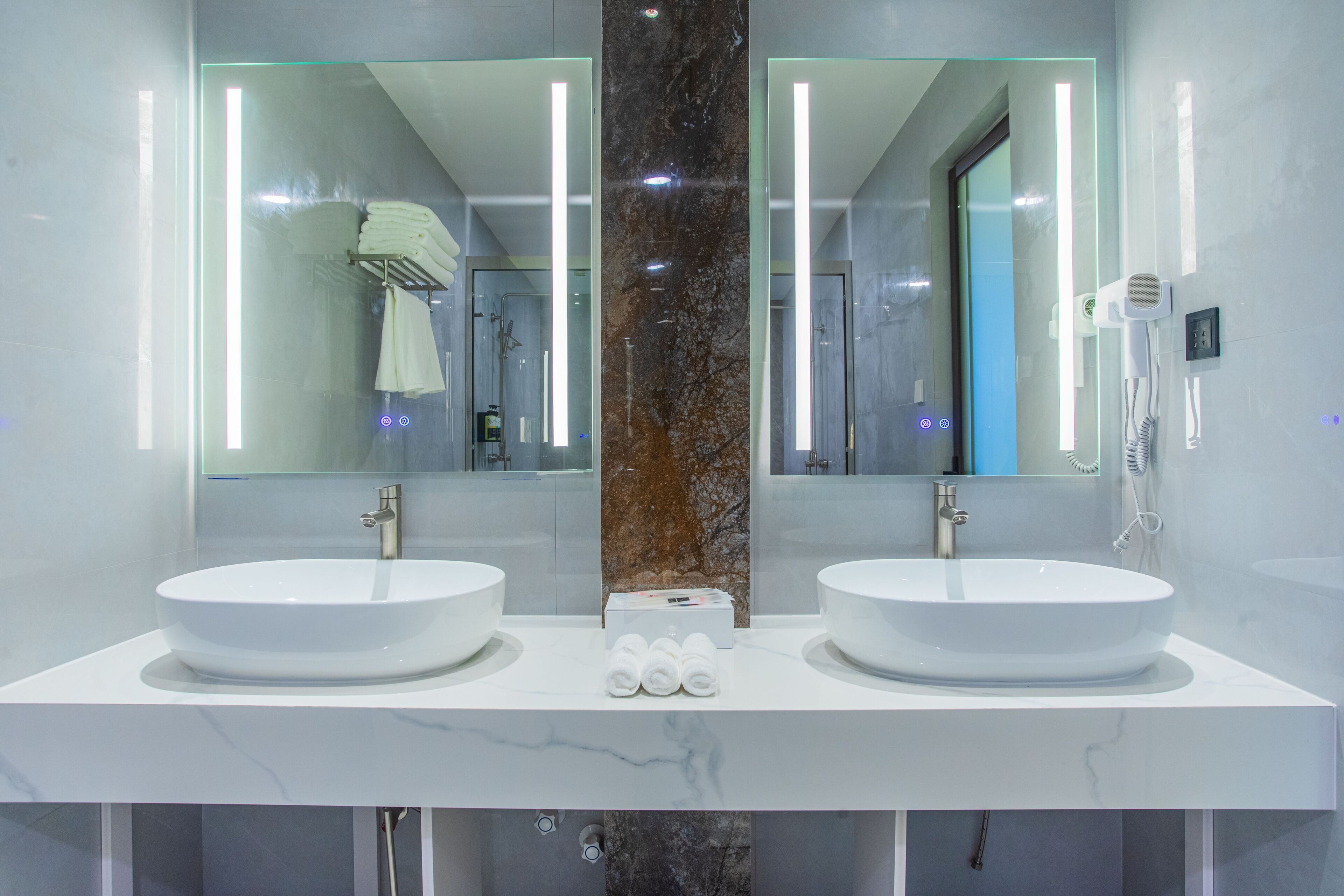 A modern bathroom with two sinks, a large mirror, and a marble column.