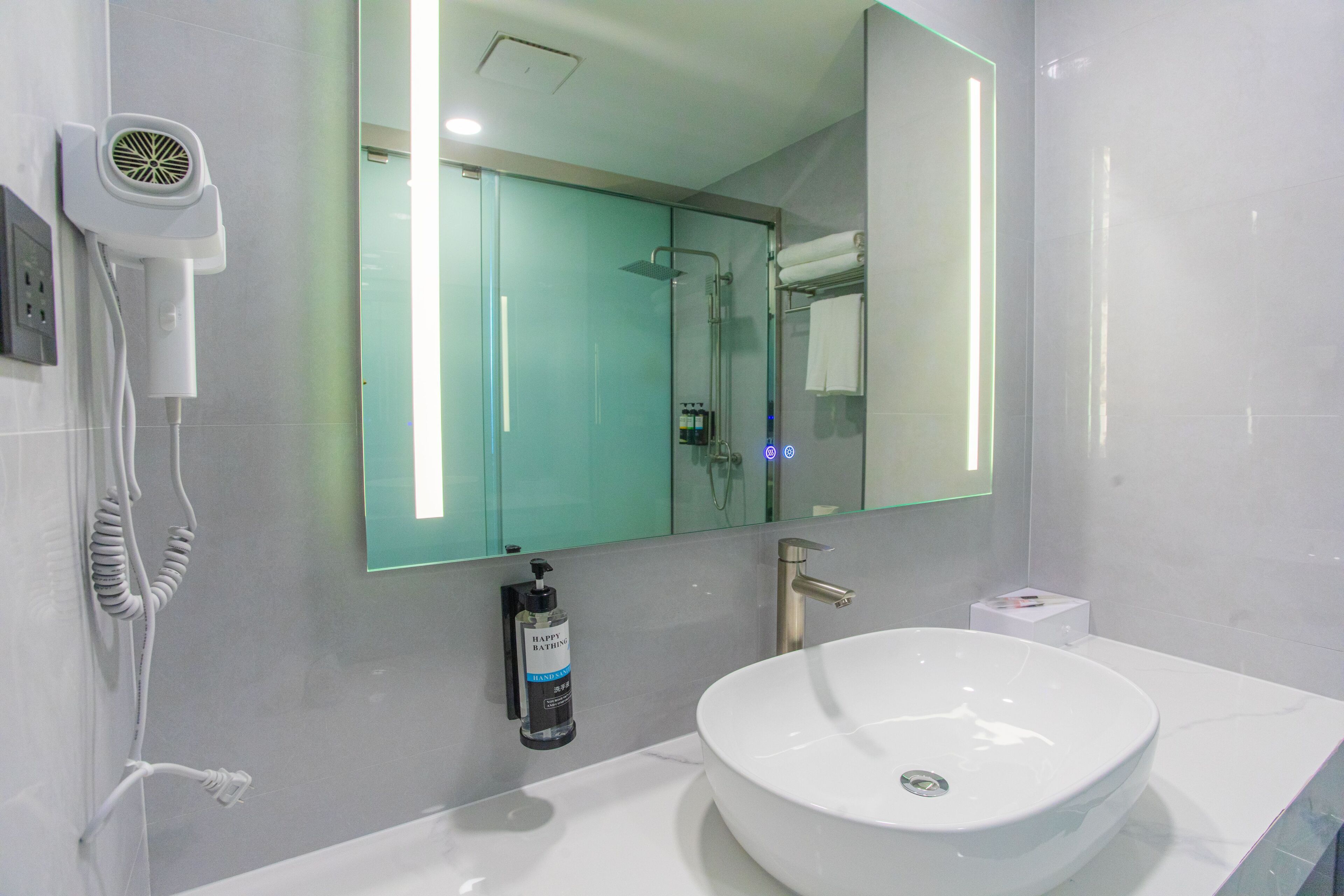 A modern bathroom with a large mirror, a white sink, and a hairdryer mounted on the wall.