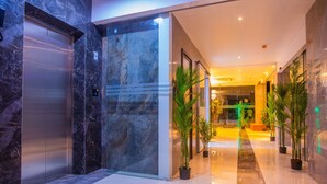 Um hall de hotel moderno com piso de mármore, um elevador e plantas em vasos.