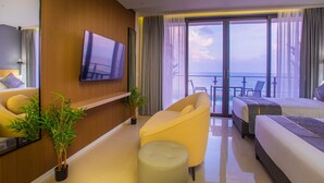 Quarto de hotel com uma janela grande, televisão de tela plana, sofá, cama e uma pequena mesa.