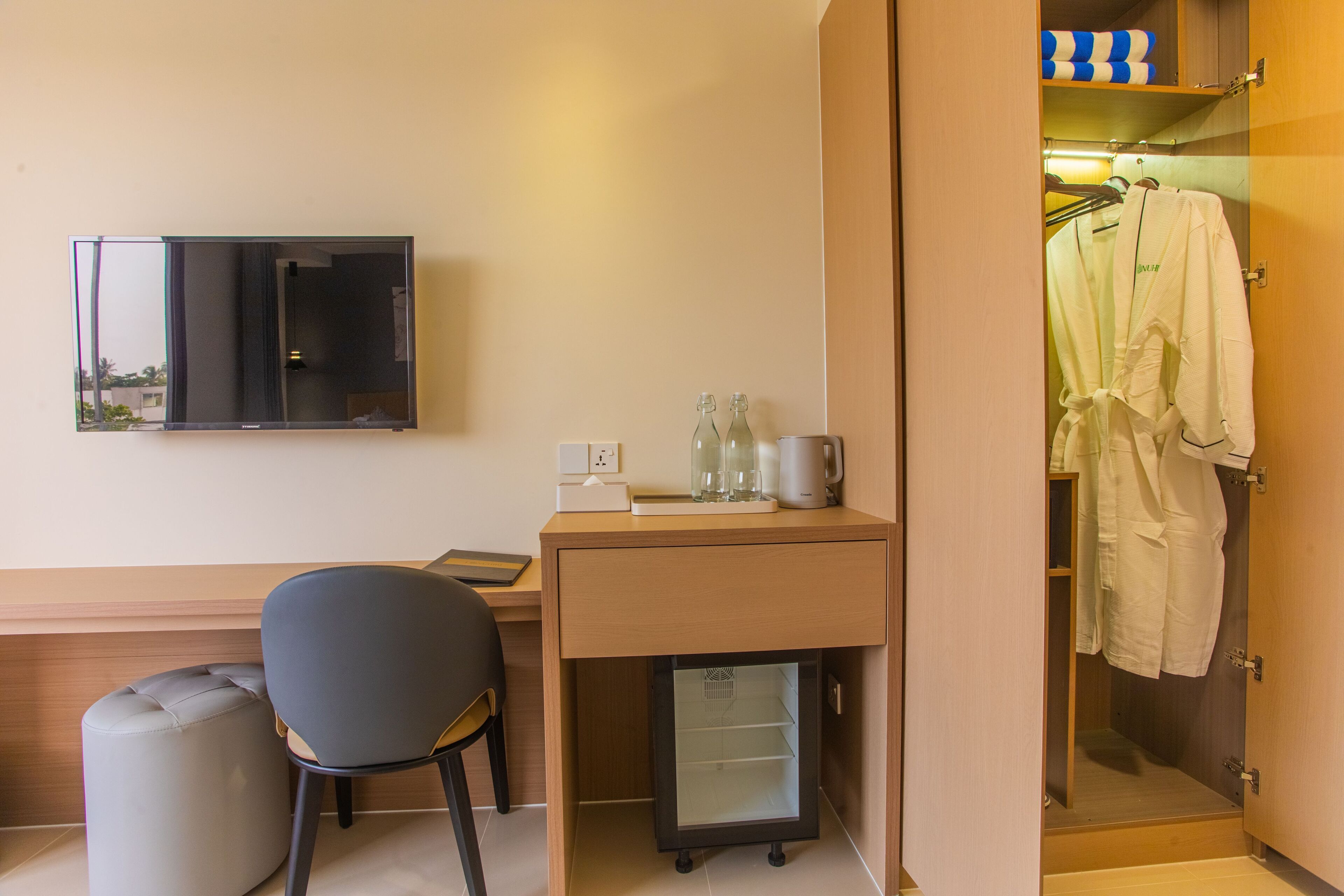 A hotel room with a desk, chair, TV, and a walk-in closet with hanging clothes.