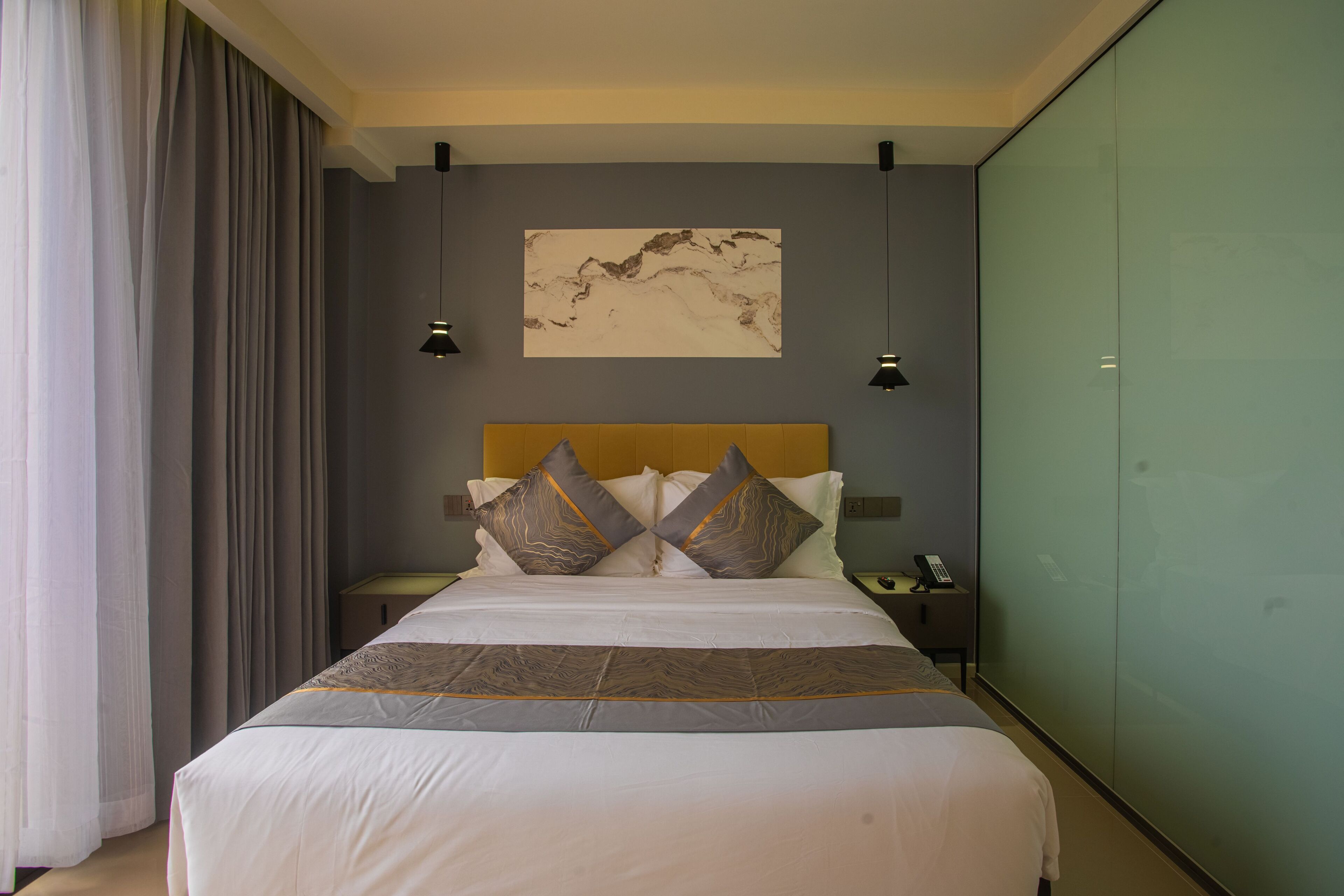 A hotel room with a large bed, a headboard, a painting on the wall, and a nightstand with a phone.