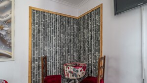 A corner room with a brick-patterned wall, a round table with floral upholstery, and two red chairs. - Suite 303 — Aquedarte Lisbon (Lisboa)