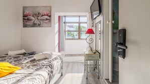 Een slaapkamer met een bed, een schilderij, een televisie, een rode lamp en een deur naar een andere kamer.