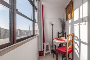 Ein Zimmer mit einem großen Fenster, einem Esstisch mit Stühlen, einem kleinen Hocker und einer Lampe.