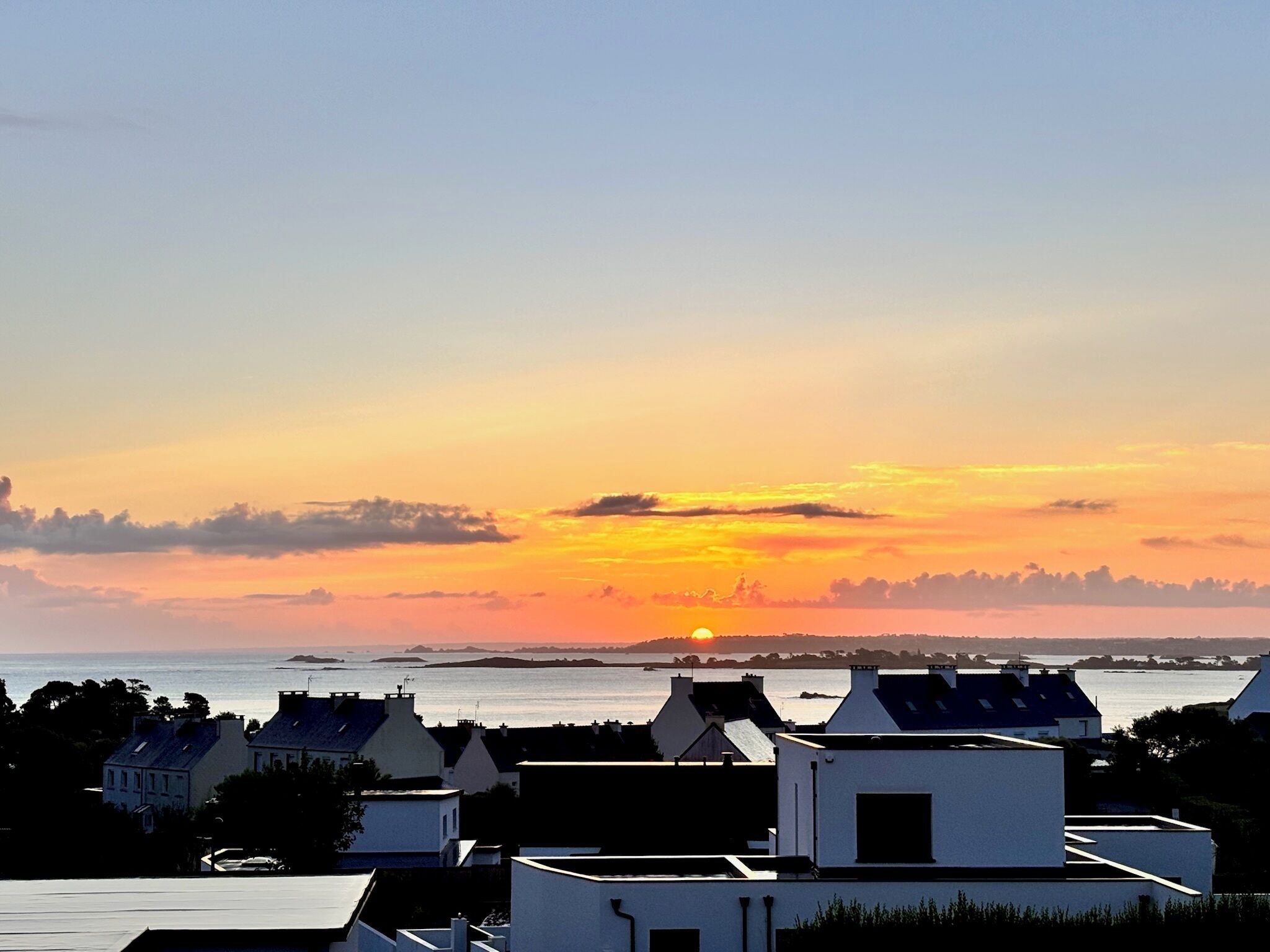 En kystby i solnedgang, med bygninger i forgrunden og udsigt over havet og fjerne øer.