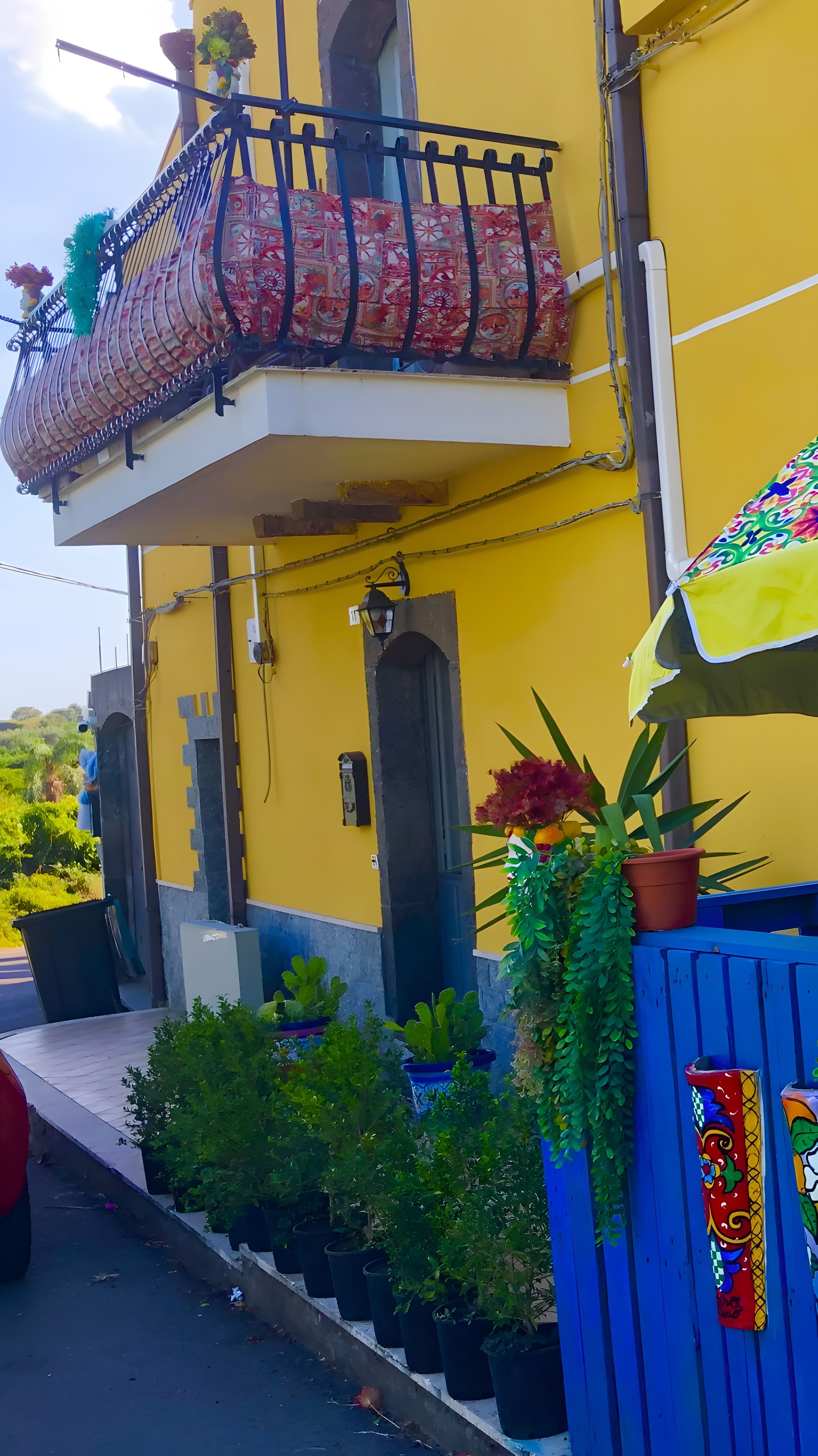 Un edificio amarillo con balcón, plantas en macetas y una valla azul.