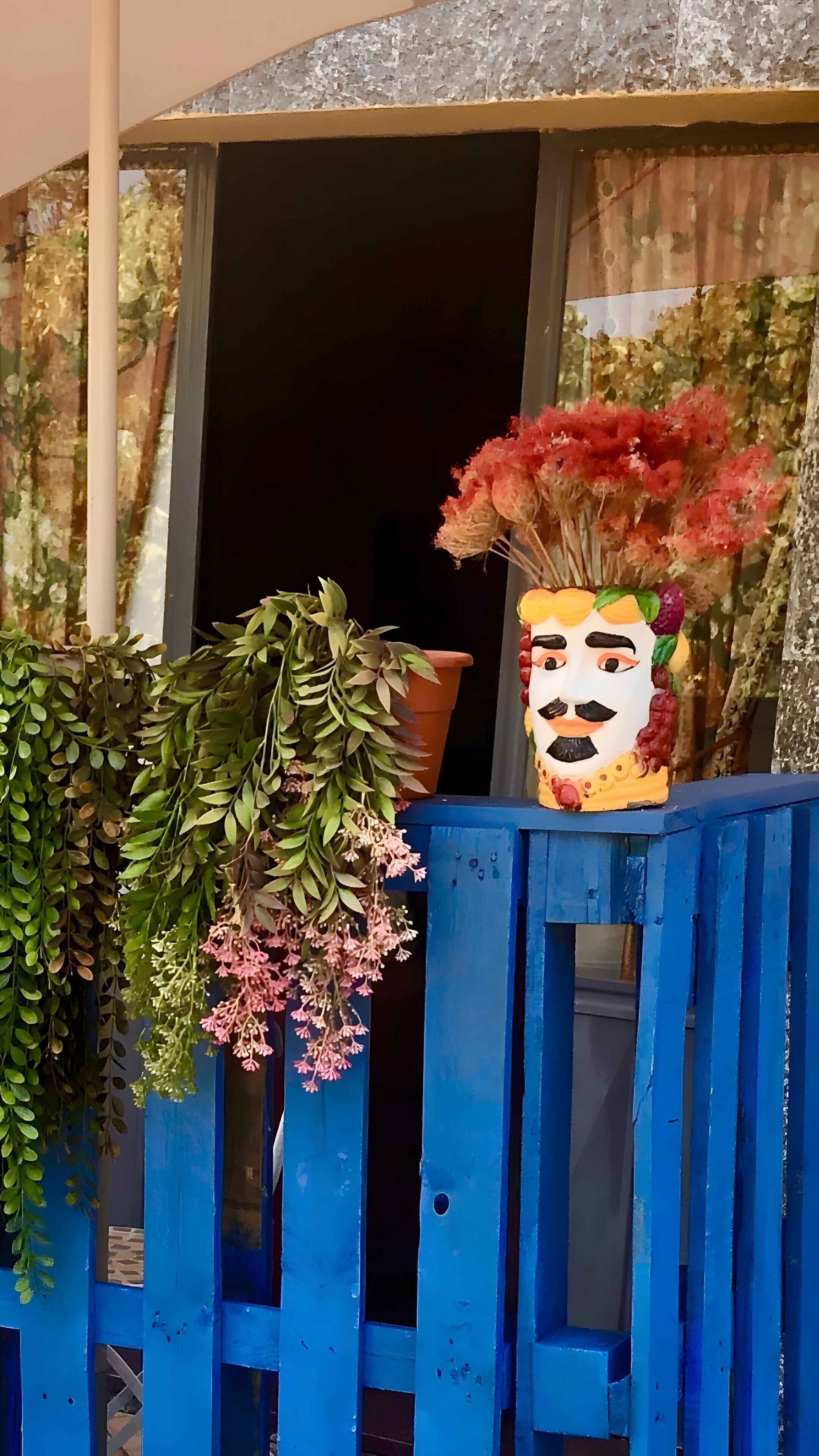 A blue fence with potted plants and a decorative item.