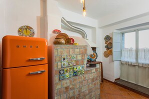 Eine Küche mit einem orangefarbenen, alten Kühlschrank, einer Ziegelwand mit bunten Fliesen und einem Fenster mit Vorhängen.