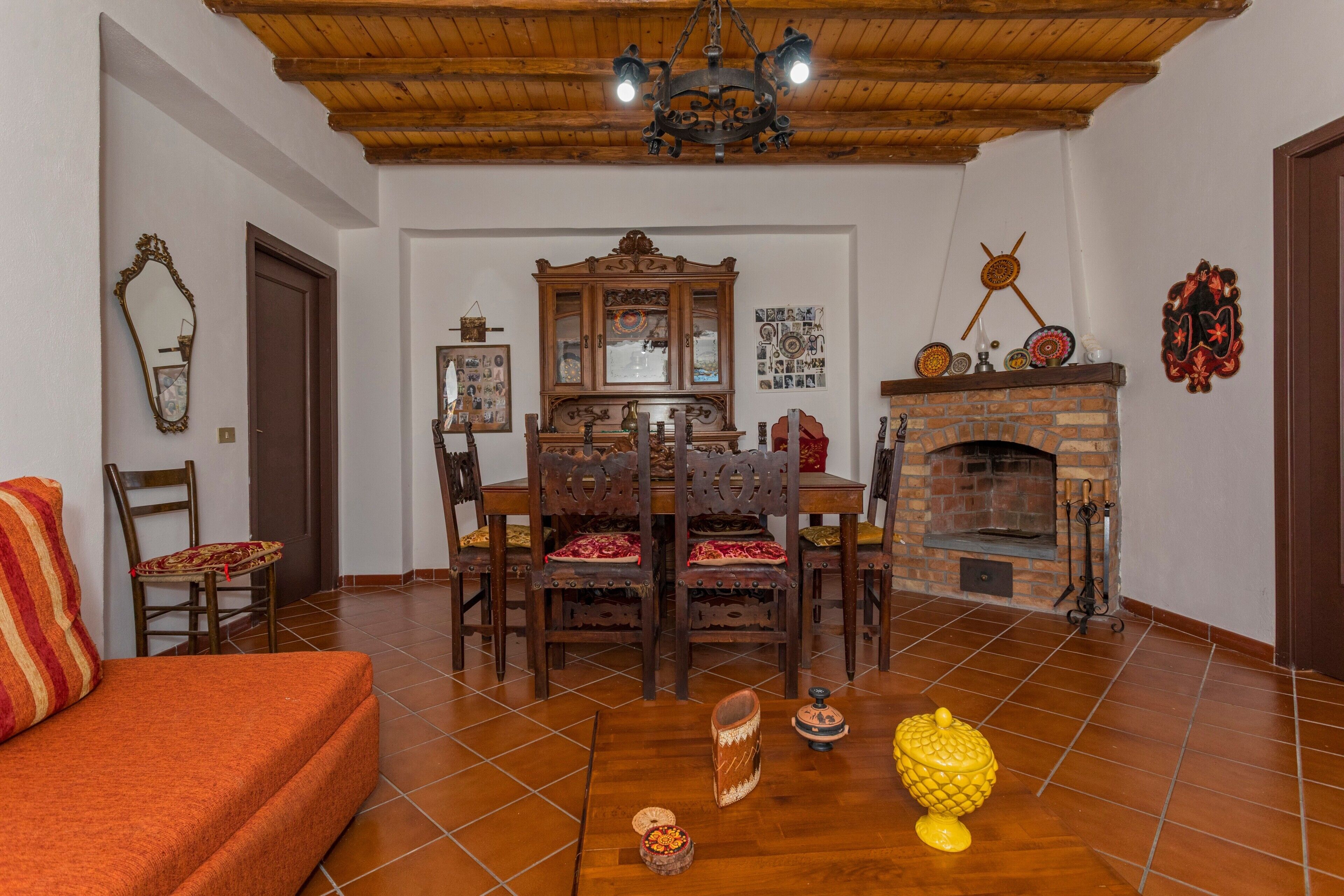 A living room with a wooden ceiling, a fireplace, a dining table with chairs, a sofa, and a mirror.