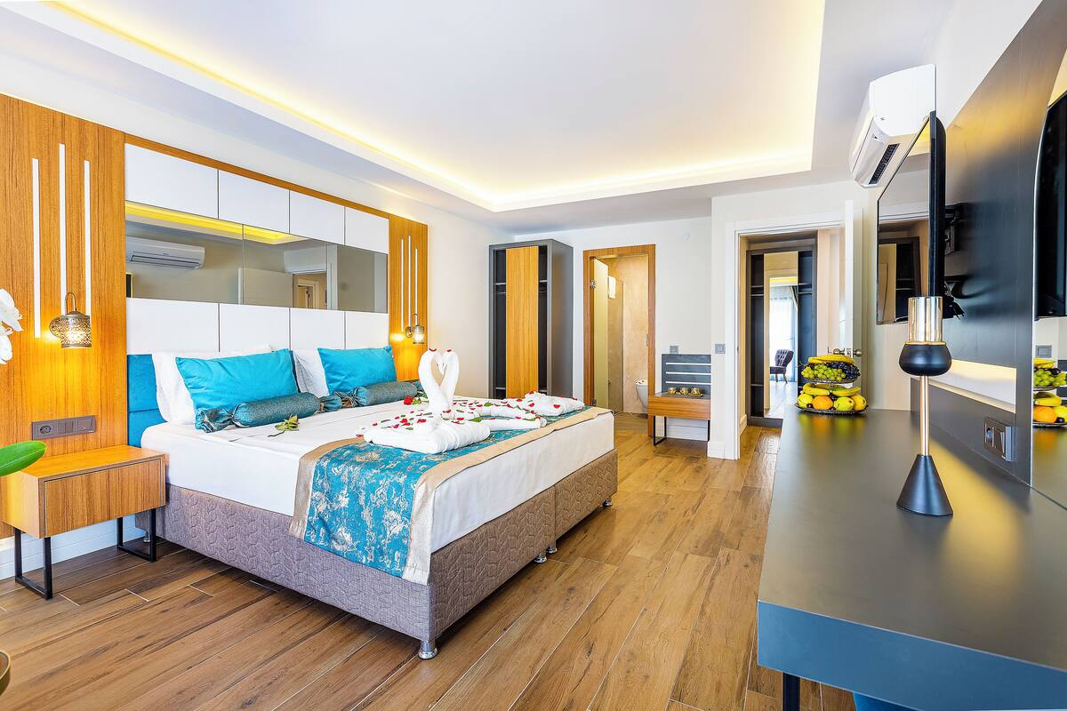A modern hotel room with a large bed, bedside tables, a flat-screen TV, and a fruit basket.