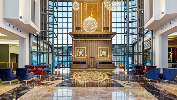 Eine großzügige Lobby mit glänzendem Marmorboden, roten und blauen Sitzgelegenheiten und einer großen Wanddekoration mit einer Uhr.