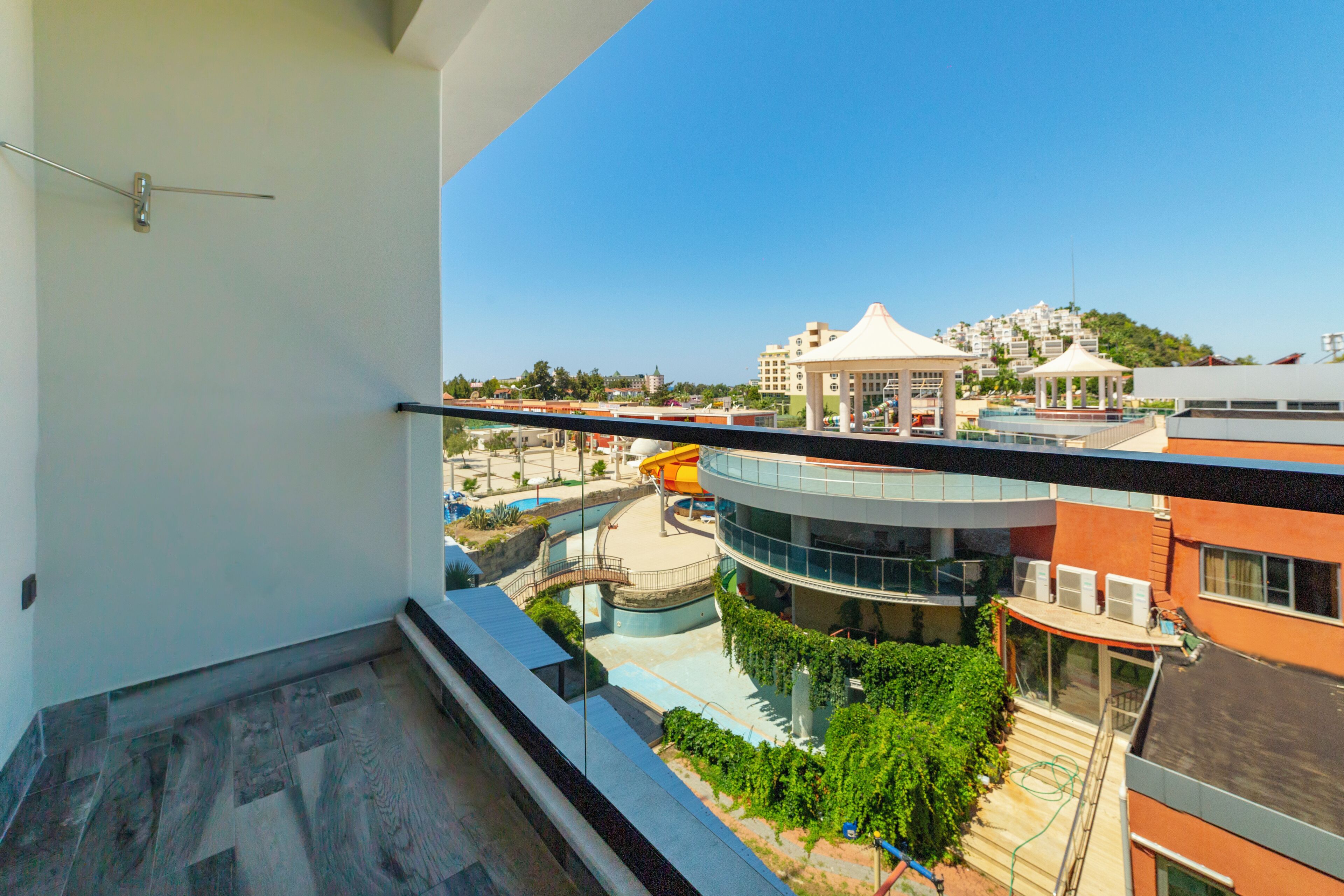 A balcony with a view of a water park, a gazebo, and buildings in the background.