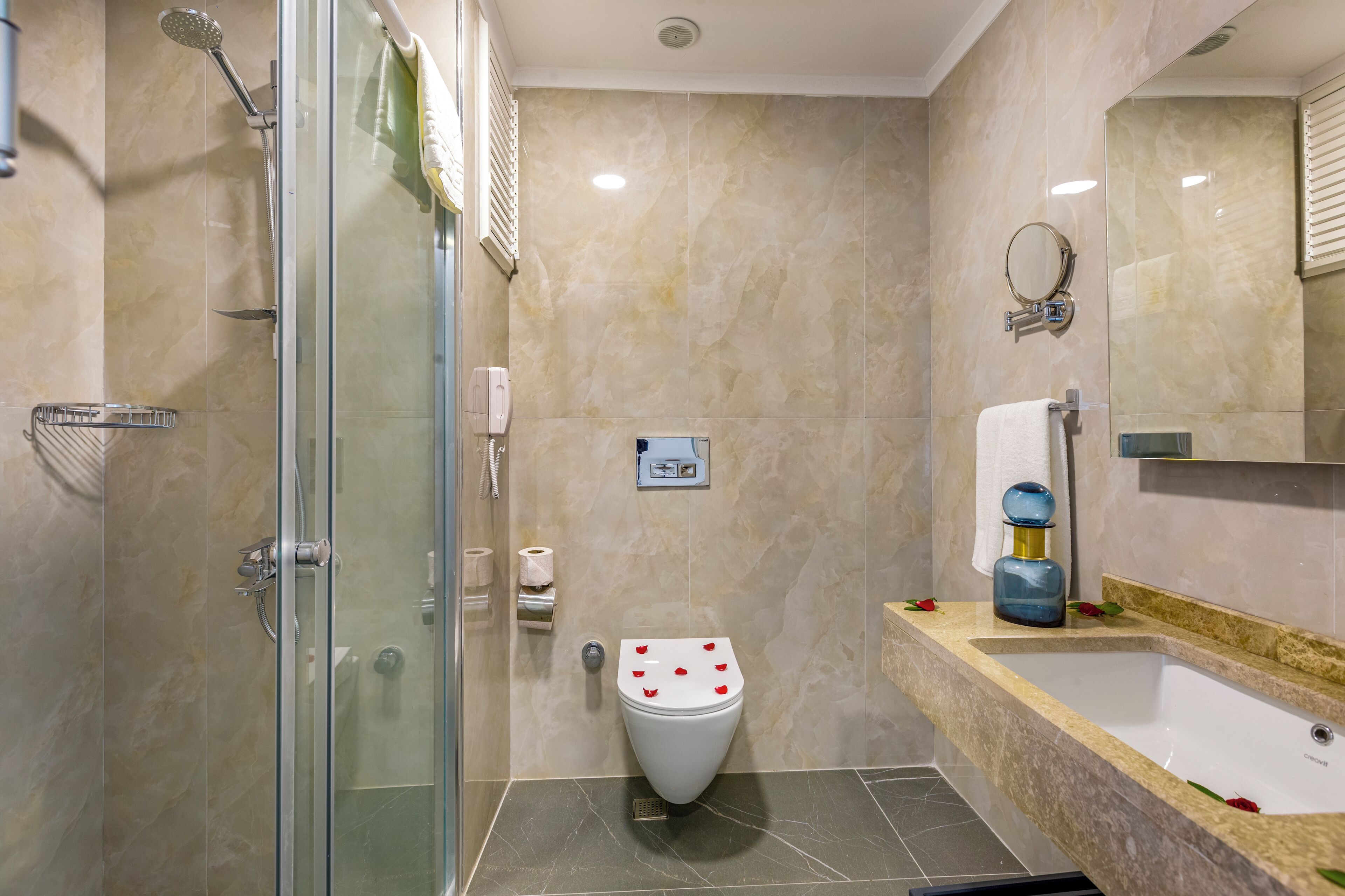 Un baño moderno con ducha envuelta en vidrio, inodoro blanco y bañera con encimera de mármol.