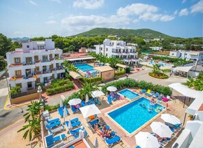 Resort com várias piscinas, espreguiçadeiras e montanhas ao fundo.