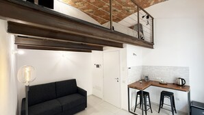 A modern kitchen with a dining area, a black sofa, and a staircase leading to an upper level. - Quadruple Room with Balcony Overlooking the Main Street and Square, Air Conditioning (Calangianus)