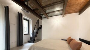 A bedroom with a bed, a staircase, and a window. - Quadruple Room with Balcony Overlooking the Main Street and Square, Air Conditioning (Calangianus)