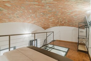 A loft-style room with a brick ceiling, a glass floor, a wooden floor, and a metal railing. - Spacious Double Room with Balcony Overlooking the Main Street and Square, Air Conditioning (Calangianus)