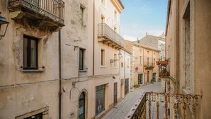 A narrow street with buildings on either side, featuring balconies, windows, and a wrought iron railing. - Quadruple Room with Balcony Overlooking the Main Street and Square, Air Conditioning (Calangianus)