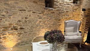 Una mesa redonda de vidrio con mantel blanco, un florero con flores y una silla tapizada de blanco en una habitación con paredes de piedra y una alfombra estampada.
