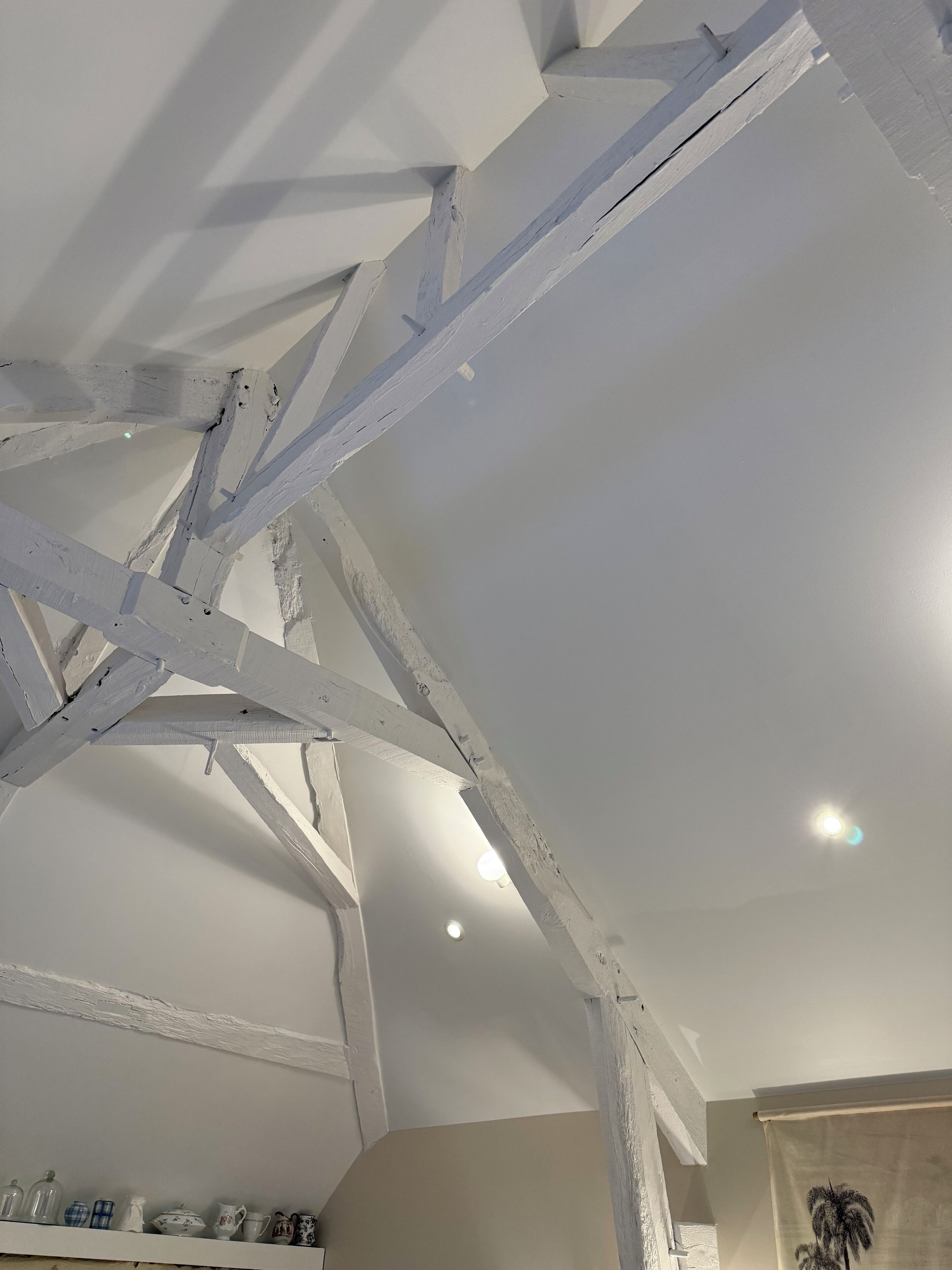 Een kamer met zichtbare houten balken, een wit plafond en een plank met diverse spullen.