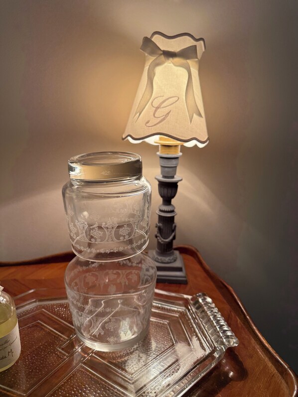 A clear glass jar with intricate designs on a wooden tray, accompanied by a lamp with a decorative shade.