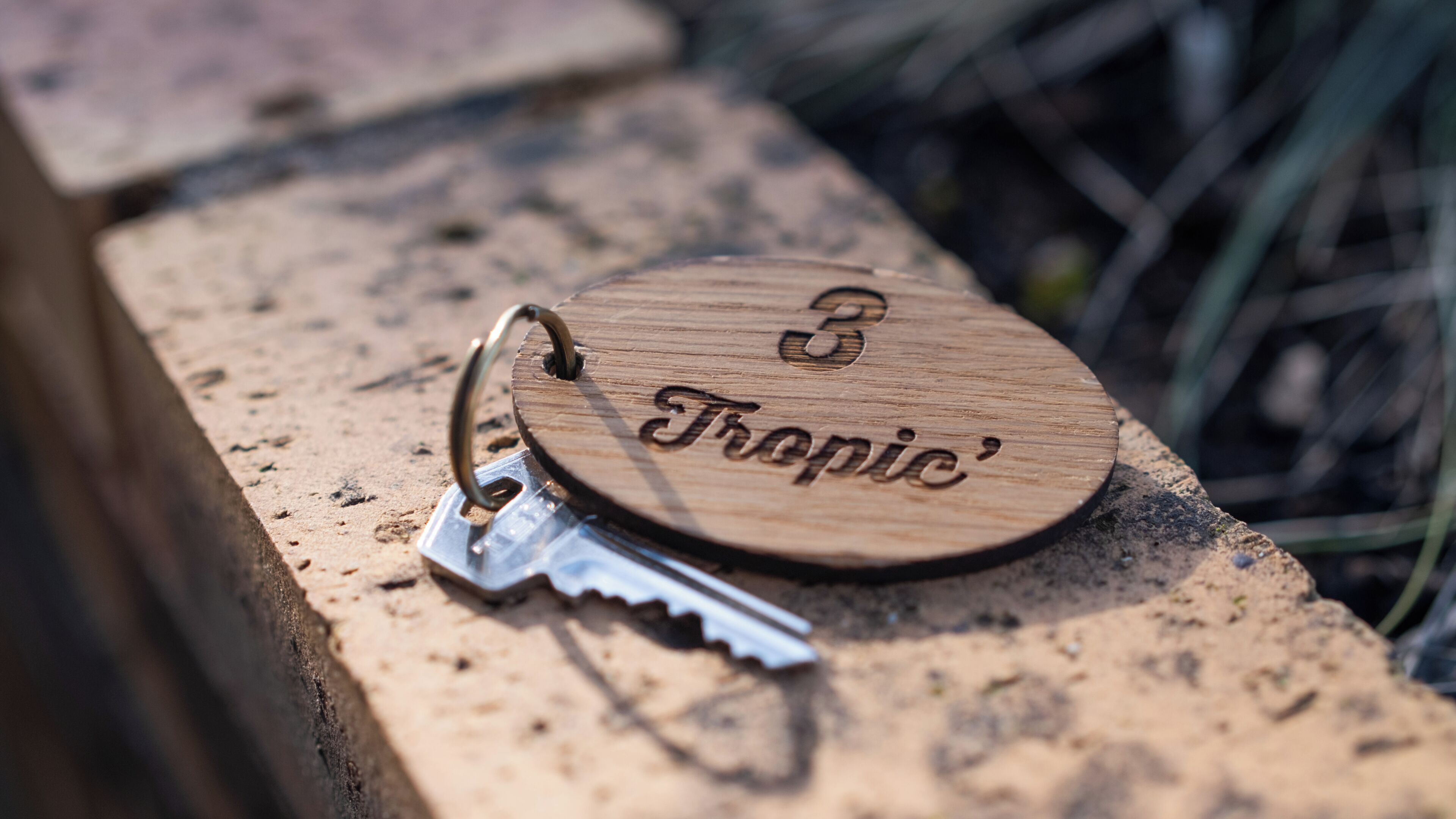 A wooden keychain with the engraving 'Tropic' and a number '3' on it, placed on a stone surface.