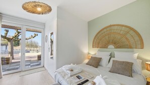 A bedroom with a bed, pillows, a bedside table, a lamp, a remote control, and a door leading to a balcony. - Chambre d'hôtes L'écrin fleuri  (Allerey-sur-Saone)
