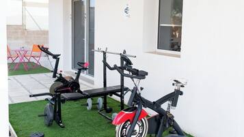 A home gym with exercise equipment, including a stationary bike, a bench press, and a weight bench, on a green artificial turf area.