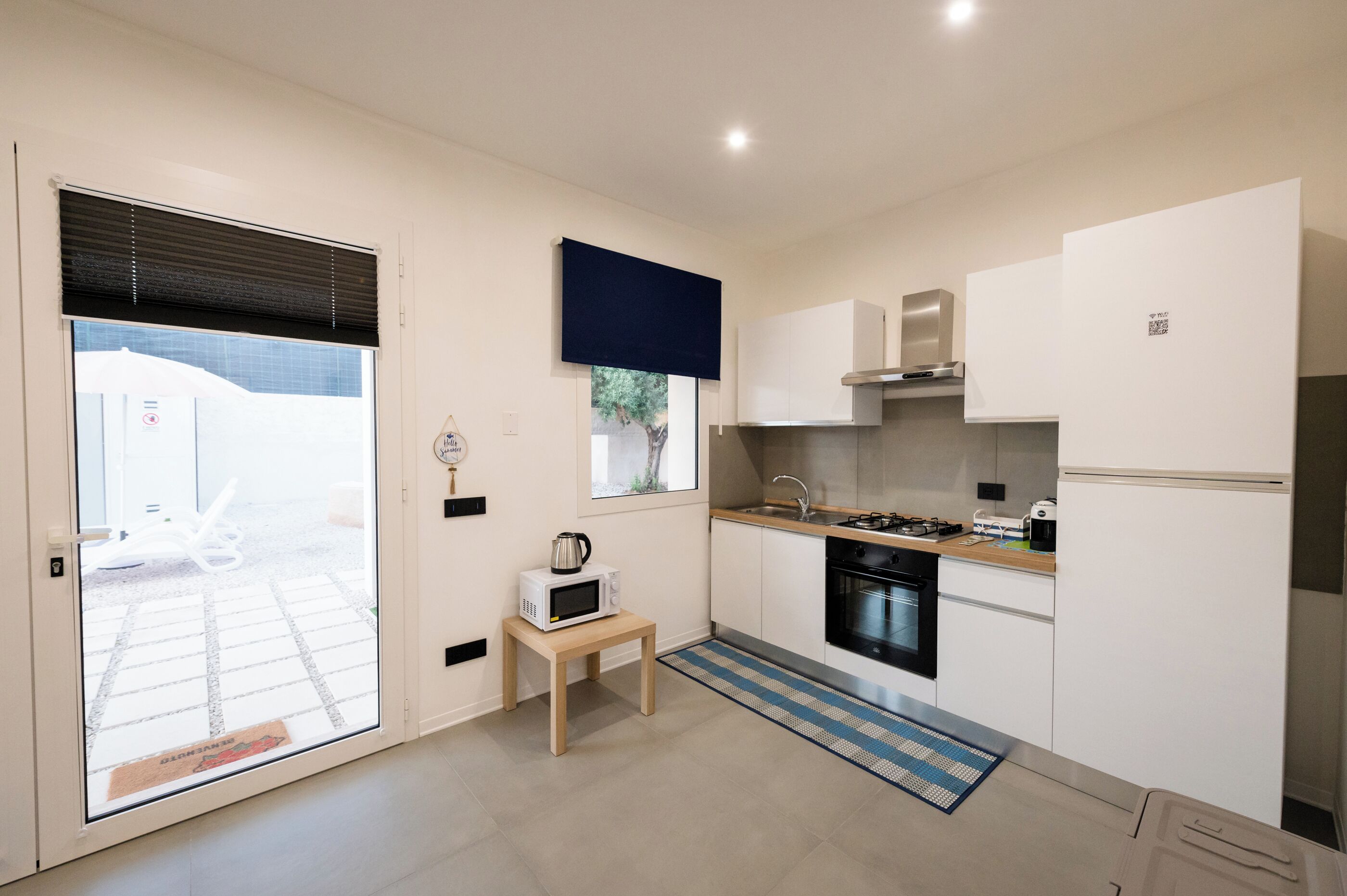 A modern kitchen with white cabinets, a microwave on a small table, a gas stove, and a refrigerator.