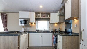 A modern kitchen with wooden cabinets, a microwave, a toaster, and a sink. - Blue Skies (Caernarfon)