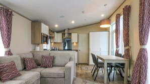 A compact living space with a sofa, a dining table, and a kitchen area. - Blue Skies (Caernarfon)