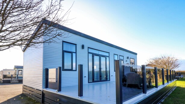 A modern mobile home with a flat roof, large windows, and a covered outdoor area. - Blue Skies (Caernarfon)