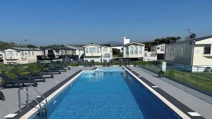 A rectangular pool with a clear blue water surface, surrounded by a black deck and a glass barrier. - Blue Skies (Caernarfon)