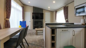 A compact kitchen with a dining area, a flat-screen TV, and a microwave. - Blue Skies (Caernarfon)