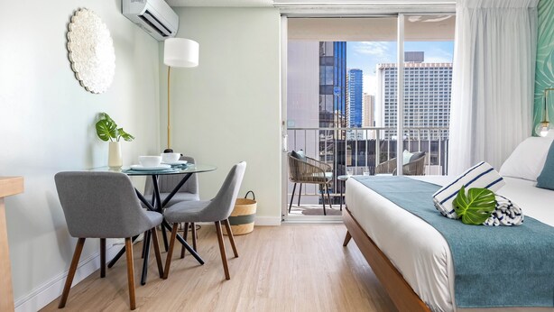 Une chambre d’hôtel moderne dotée d’un balcon, d’un coin repas et d’un lit offrant une vue sur le paysage urbain.