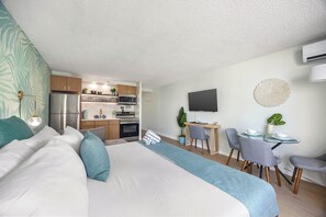 A modern hotel room with a bed, a desk, a dining table, and a kitchenette.