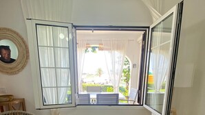 A room with a large window, a round wicker chair with a pillow, two small white tables, and a white ceiling fan. - Casa Carlito 153 - zone 3 Son Bou (San Jaime Mediterráneo)